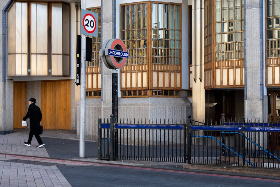 A rectangular white sign mounted on a brick wall, displaying the text 'Welcome to South Kensington SW7' in black and red letters. The brick wall has a textured surface with varies shades of reddish-brown bricks, some with visible mortar lines. The sign is positioned centrally on the wall, with metal fasteners at each corner, and appears clean and well-maintained, indicating an area in South Kensington, Kensington. The scene is well-lit, with natural lighting highlighting the brick textures and the contrast of the sign's colors, reflecting a tidy and organized outdoor setting as part of internal or external surface cleaning and maintenance by Deep Cleaning Kensington.