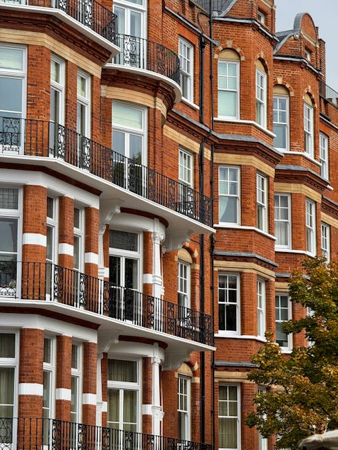 Close-up view of the exterior of a multi-story red brick residential building in Kensington, featuring large sash windows with white frames and decorative white stone accents. The building has black w